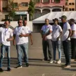 Group of event staff in white shirts standing in a parking lot, one man gesturing as he speaks near a white tent.