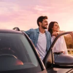 Couple leaning out of an open car door at sunset, smiling and enjoying the view.