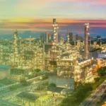 JDIDA-IMPROV-1200x873 1 1 - Agence 47 Industrial refinery complex at sunset with tall processing towers and numerous illuminated pipes.