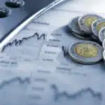 Calculator beside a financial chart and a pile of coins, symbolizing money and market analysis.