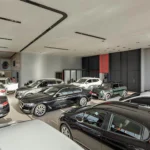 Indoor car showroom with multiple cars on display and Otoclic branding on the wall, bright showroom lighting above.