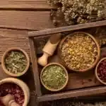 Top-down view of a wooden spice tray with bowls of dried herbs and spices on a rustic wooden table.