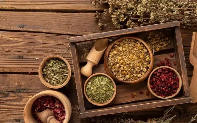 Top-down view of a wooden spice tray with bowls of dried herbs and spices on a rustic wooden table.