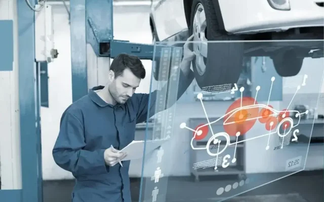 Mechanic in blue coveralls reviews a paper beside a car on a lift, with a translucent holographic car diagram in view.
